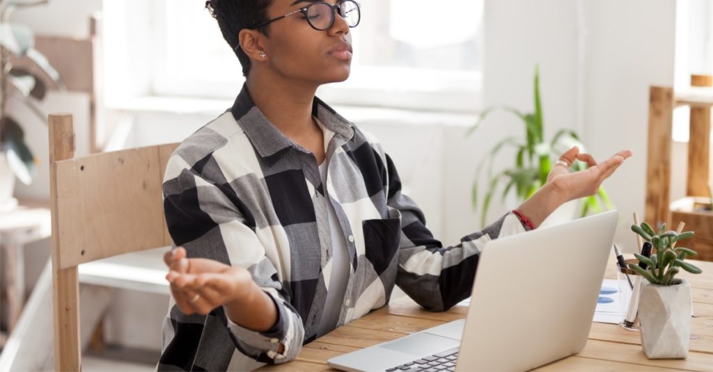 African American female in glasses meditate at workplace control emotions